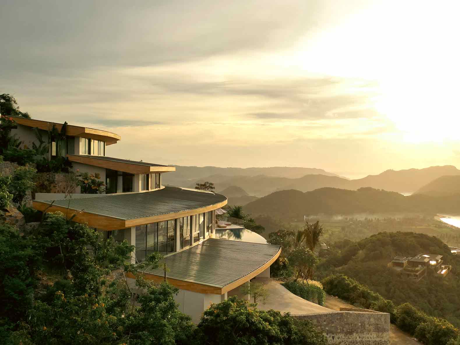 Curved roofline of a cliffside villa by this Sumbawa architect overlooks layered hills at sunset.