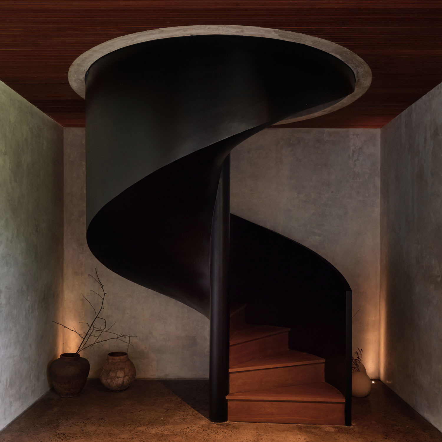 Sculptural black spiral staircase leads to timber steps inside a Sumbawa architect's villa.